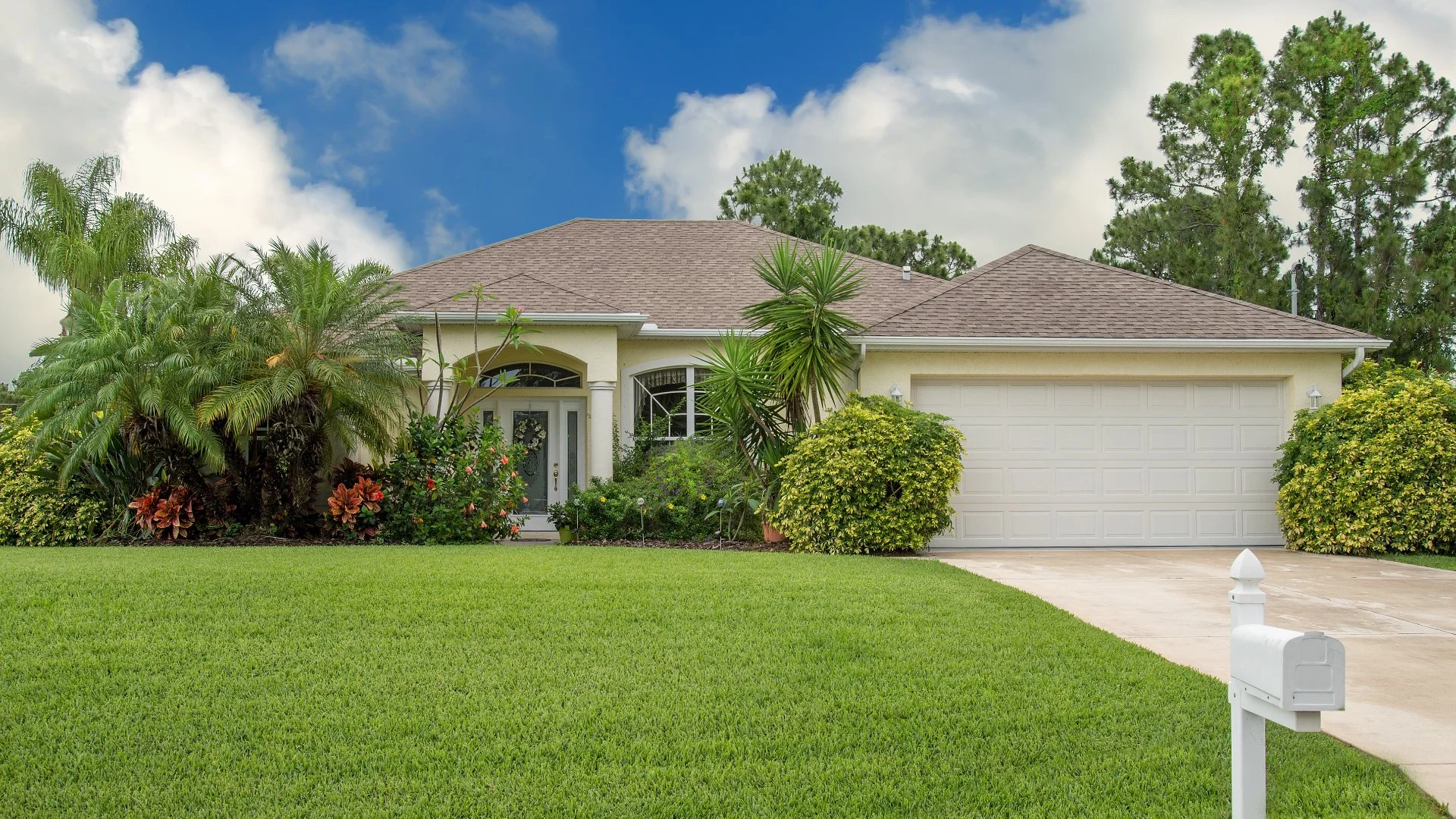 Single-story house with attached garage, lush greenery, and a white mailbox on a sunny day in West Palm Beach, FL.